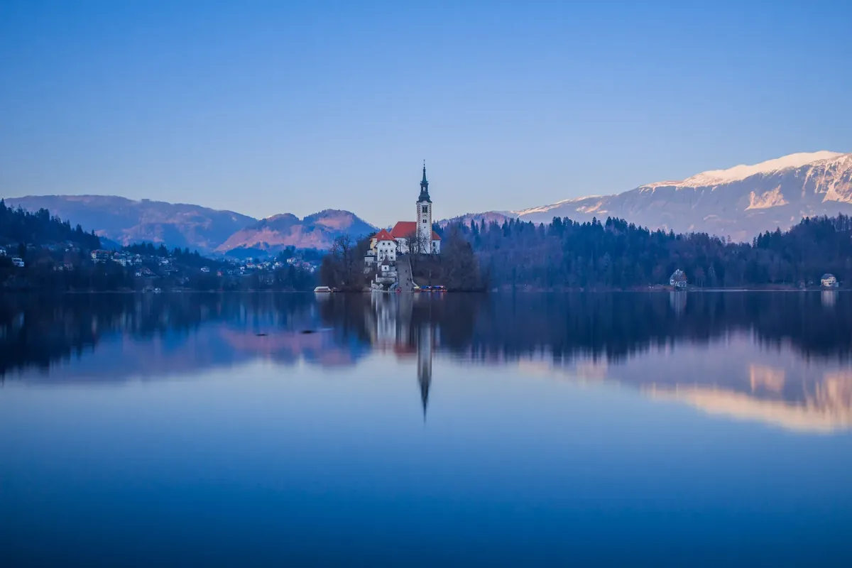 Bled Island and the church reflected in Lake Bled with mountains in the background