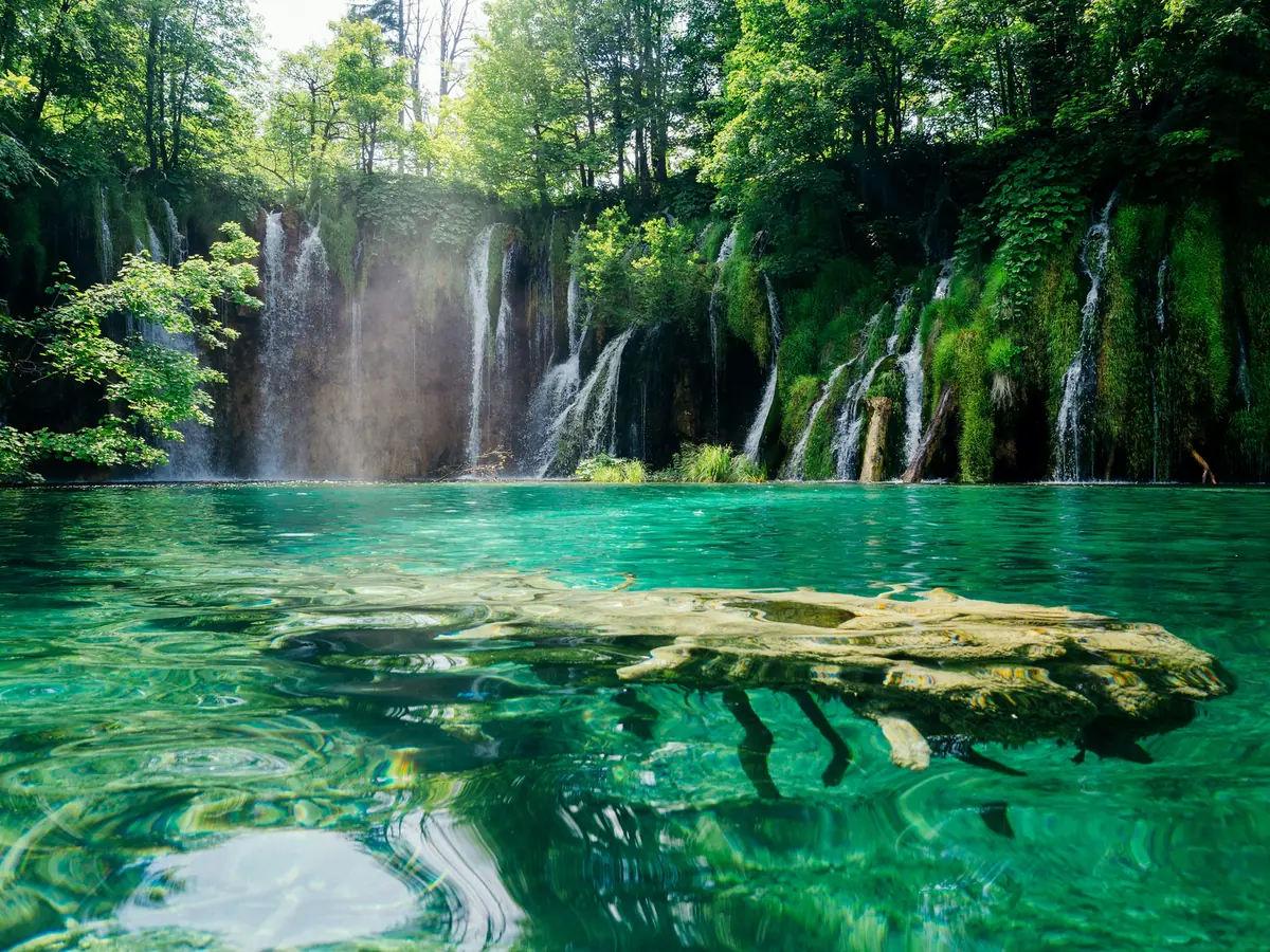 Waterfalls flowing into turquoise water beneath green forest at Plitvice Lakes National Park